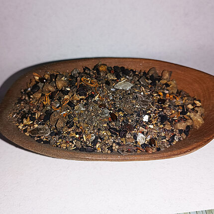 Coarse dark incense blend with seeds, dried fragments and translucent pieces in a wooden spoon
