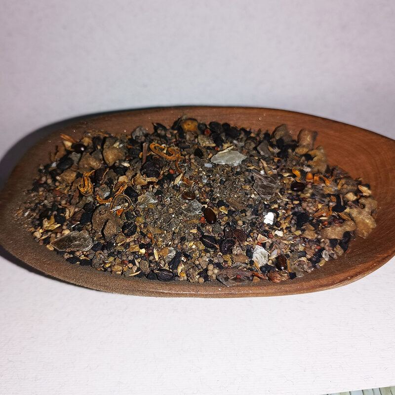 Coarse dark incense blend with seeds, dried fragments and translucent pieces in a wooden spoon