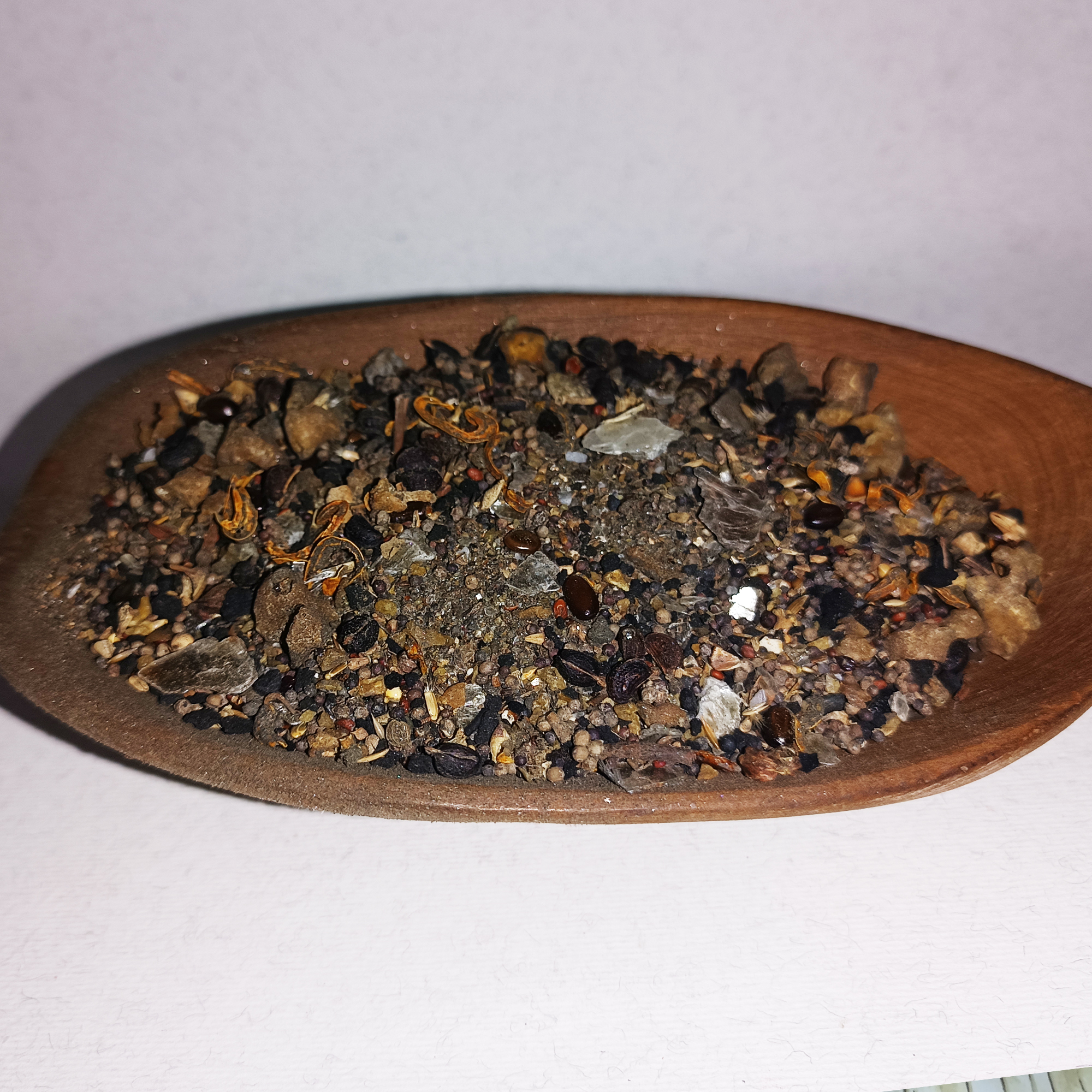 001-v-4 Coarse dark incense blend with seeds, dried fragments and translucent pieces in a wooden spoon