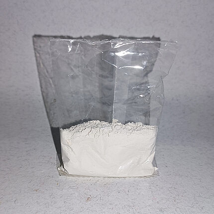 Clear pouch of loose, fine off-white kaolin powder against a pale background