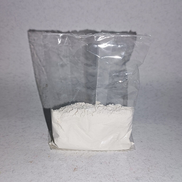 Clear pouch of loose, fine off-white kaolin powder against a pale background