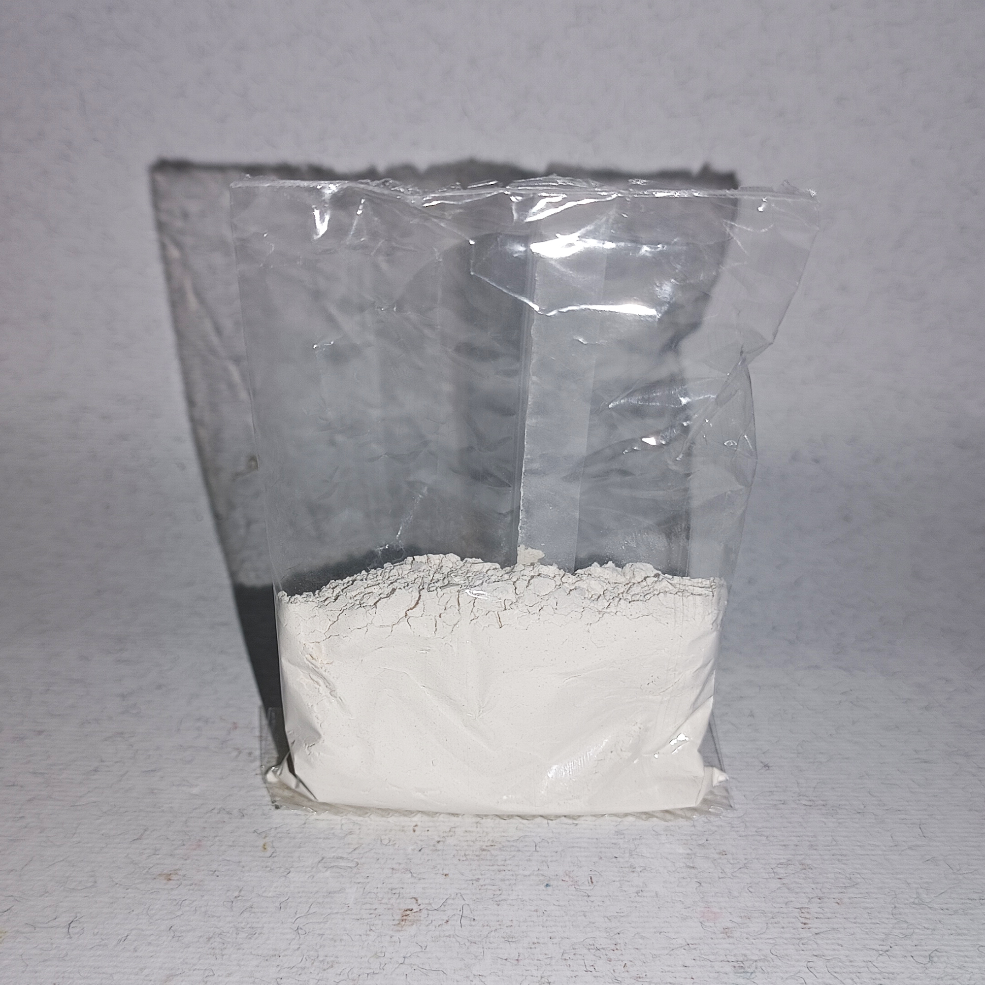 001-v-45 Clear pouch of loose, fine off-white kaolin powder against a pale background