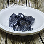 Dark metallic mineral kohl stones with loose black powder in a white bowl.