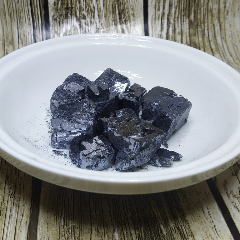 Dark metallic mineral kohl stones with loose black powder in a white bowl.