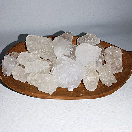 Translucent white alum stone chunks on a round wooden dish against a white background