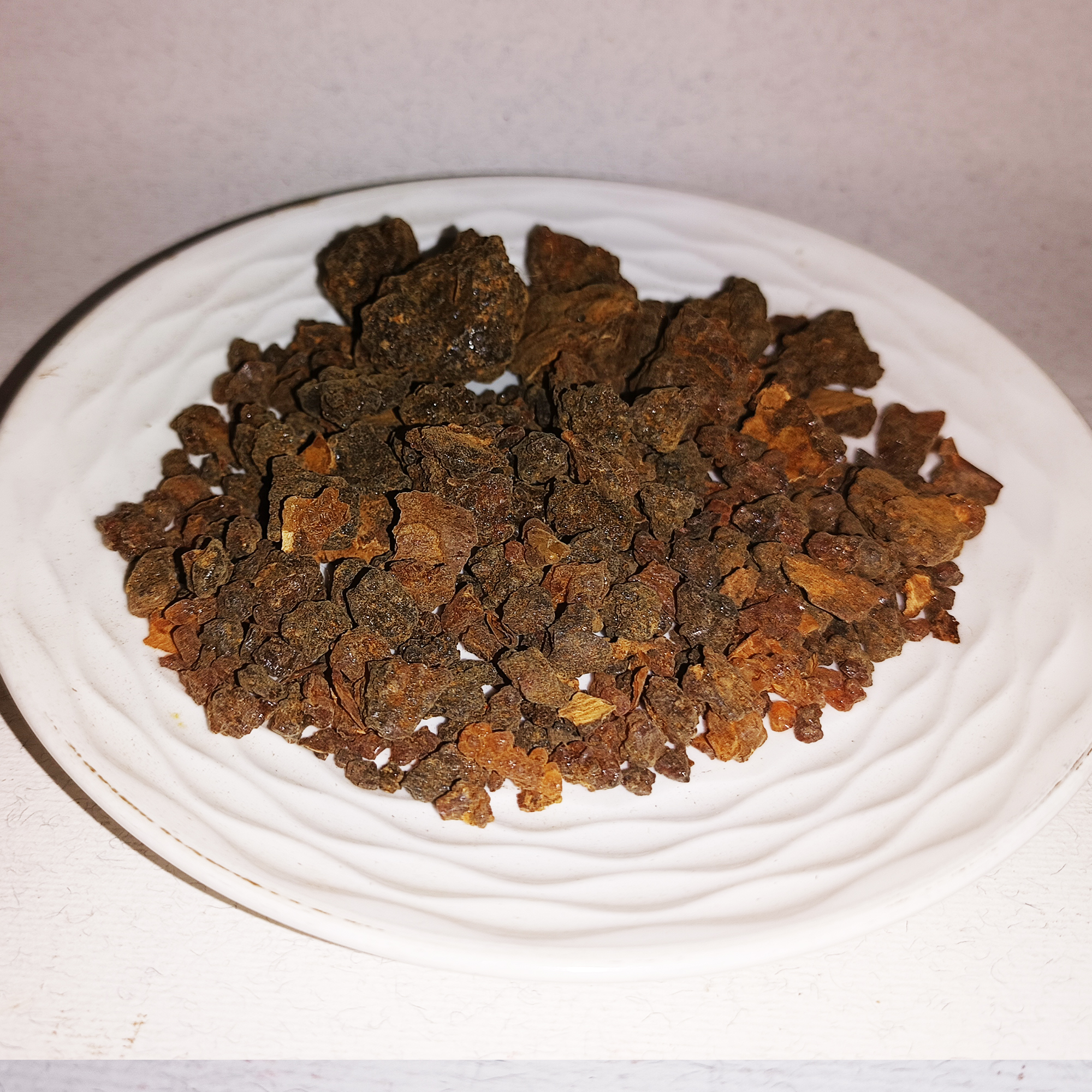 001-v-50 Morceaux de résine de myrrhe bruns et ambrés disposés sur une assiette blanche en céramique.