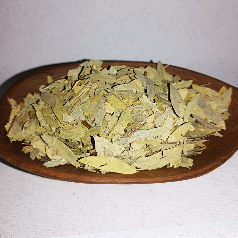 Pale green dried senna leaves spread in a round wooden dish