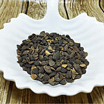 Dark brown Staphisagria seeds in a white leaf-shaped dish on a wooden surface