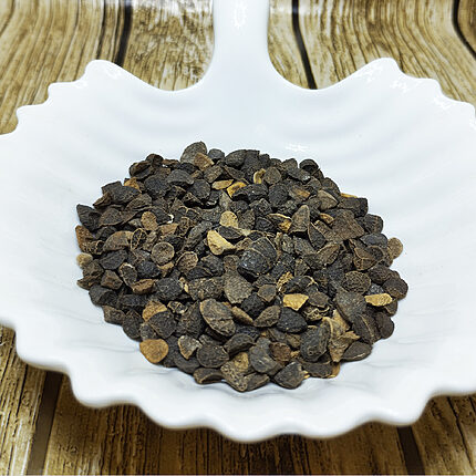 Dark brown Staphisagria seeds in a white leaf-shaped dish on a wooden surface