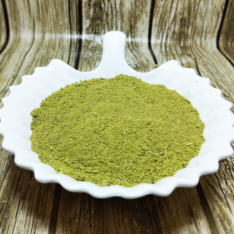 Fine green Tabrima herbal powder in a white scalloped dish on a wood-patterned surface