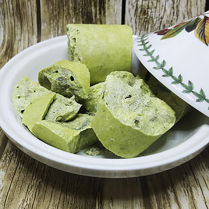 Bright yellow-green sulfur chunks with rough broken faces on a white plate beside a floral-patterned dish