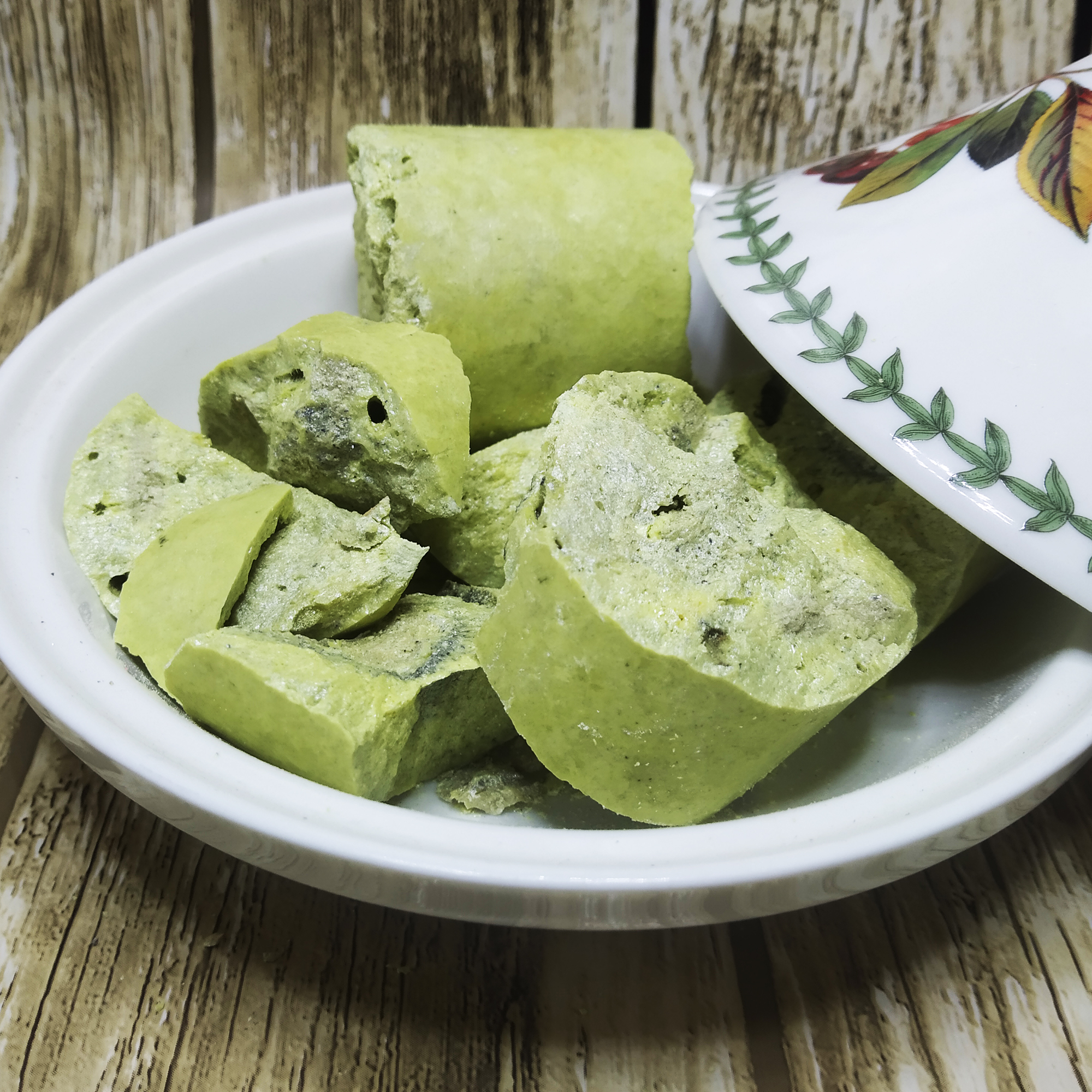 001-v-59 Bright yellow-green sulfur chunks with rough broken faces on a white plate beside a floral-patterned dish