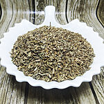 Loose dried carrot seeds piled in a white dish on a wood-grain surface