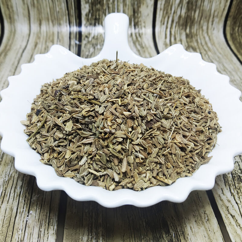 Loose dried carrot seeds piled in a white dish on a wood-grain surface