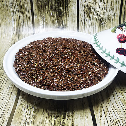 Glossy brown flax seeds piled in a white dish on a wood-grain surface
