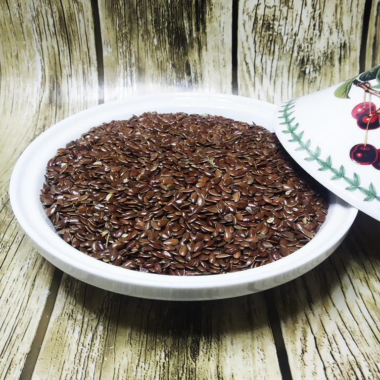 Glossy brown flax seeds piled in a white dish on a wood-grain surface