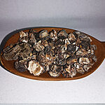 Dark dried amla fruit pieces piled on an oval wooden dish