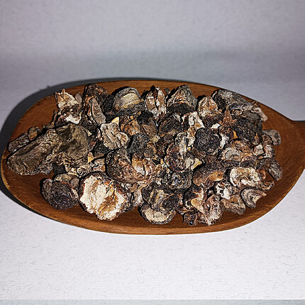 Dark dried amla fruit pieces piled on an oval wooden dish