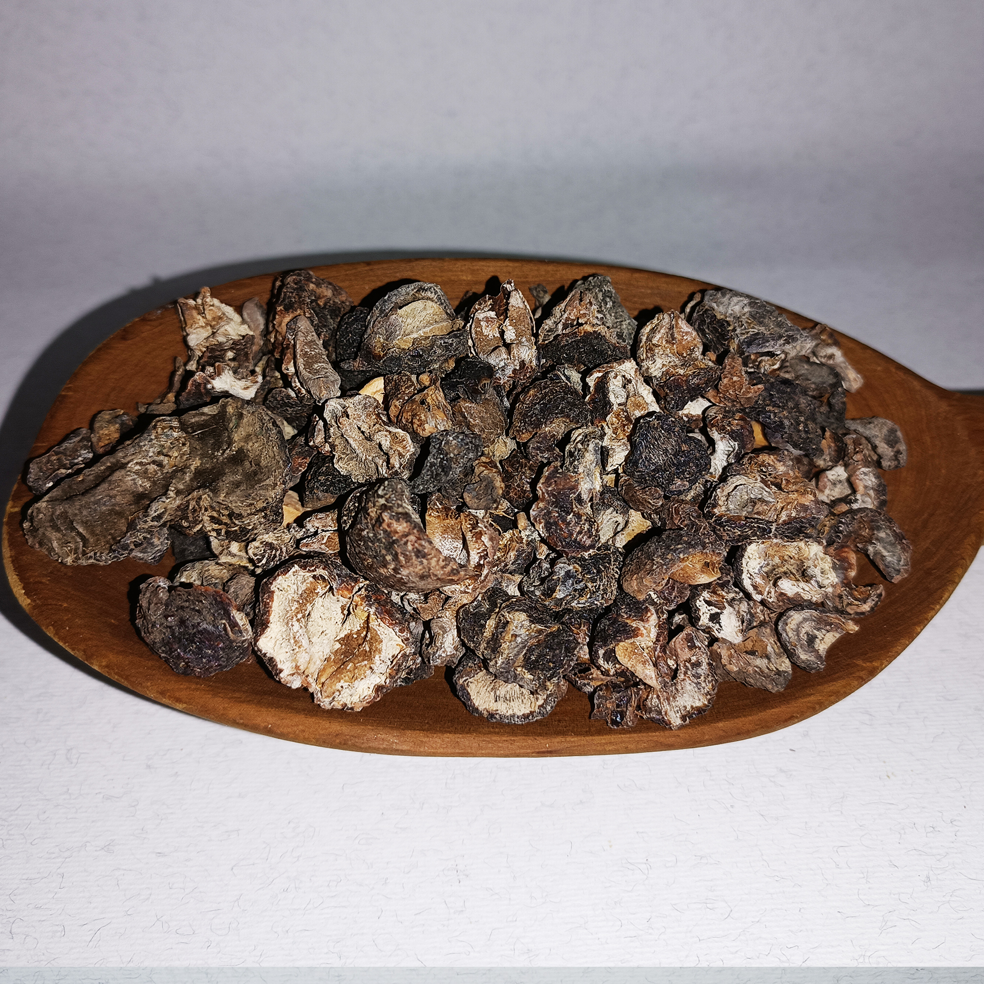 001-v-65 Dark dried amla fruit pieces piled on an oval wooden dish