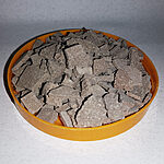 Grey-brown dry rhassoul clay pieces in a round orange dish.