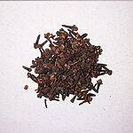 Pile of whole dried cloves on a white textured surface