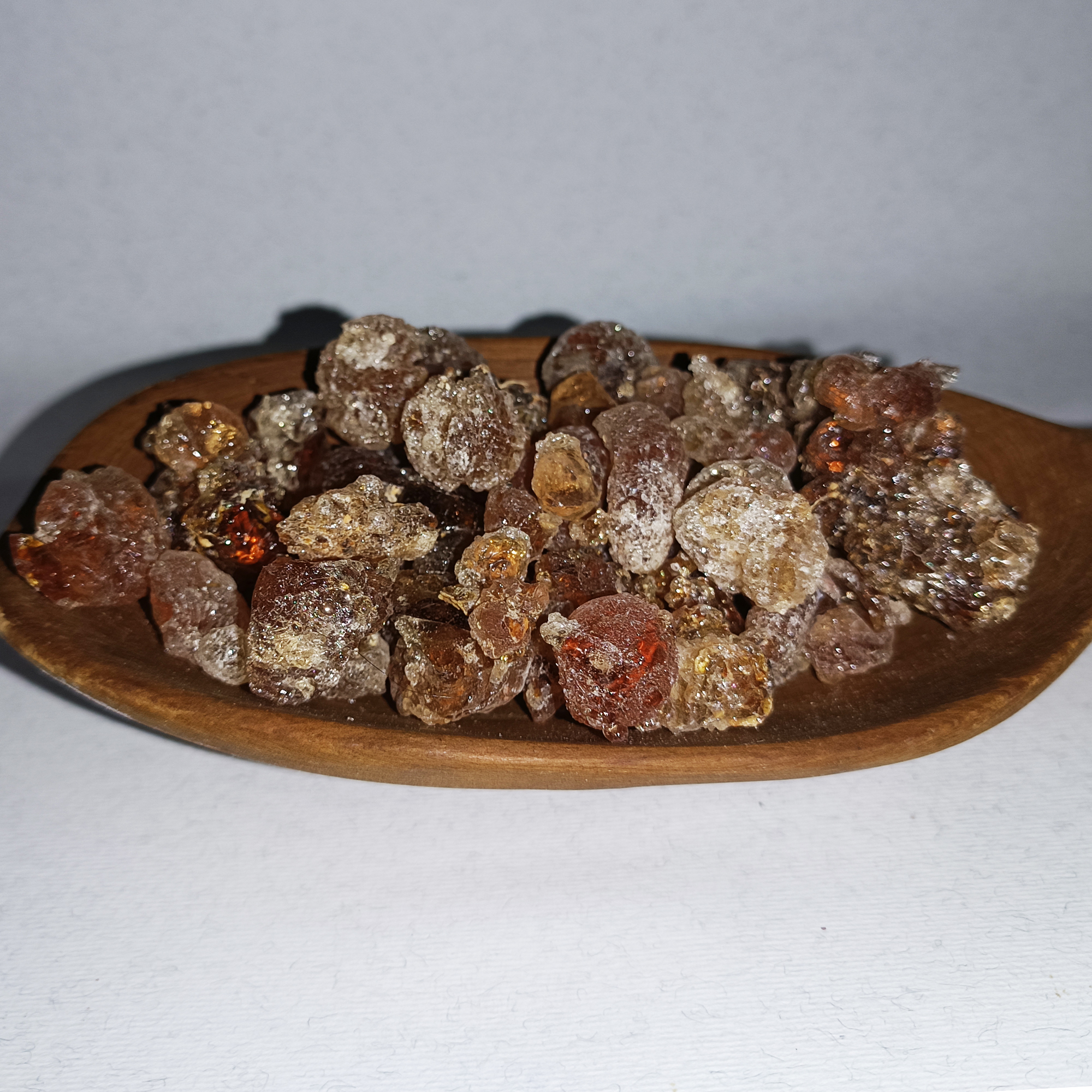 001-v-71 Clear, amber and reddish gum Arabic resin tears arranged on a round wooden plate.