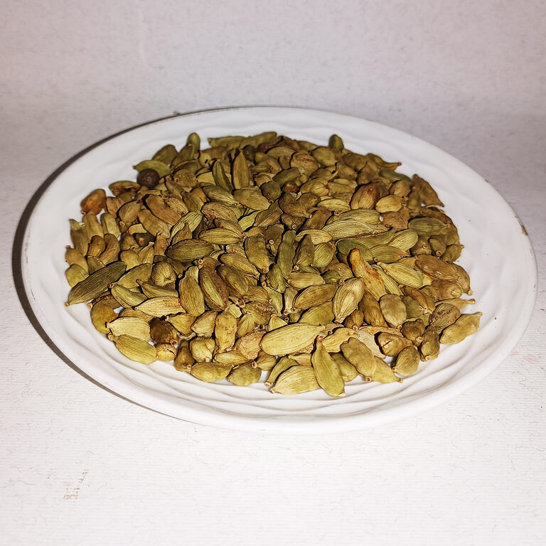 Whole green cardamom pods piled on a white plate