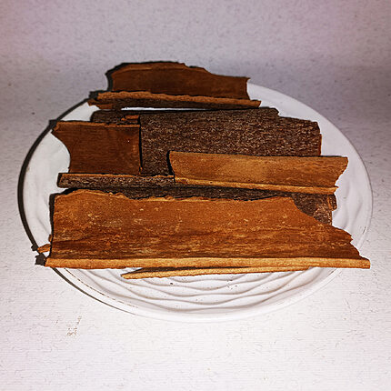 Brown cinnamon bark strips stacked on a white plate
