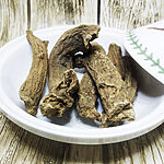 Several coarse dried Indian costus root pieces arranged on a white plate against a wood-grain background.