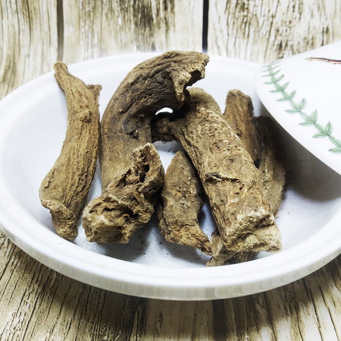 Several coarse dried Indian costus root pieces arranged on a white plate against a wood-grain background.