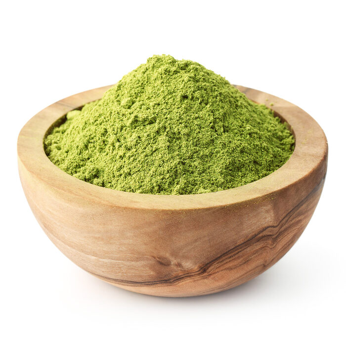 Poudre de henné verte et fine en monticule dans un bol rond en bois sur fond blanc
