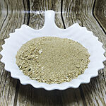 Light greenish-beige ground Sarghina powder heaped on a white scalloped dish over a wood-grain surface.