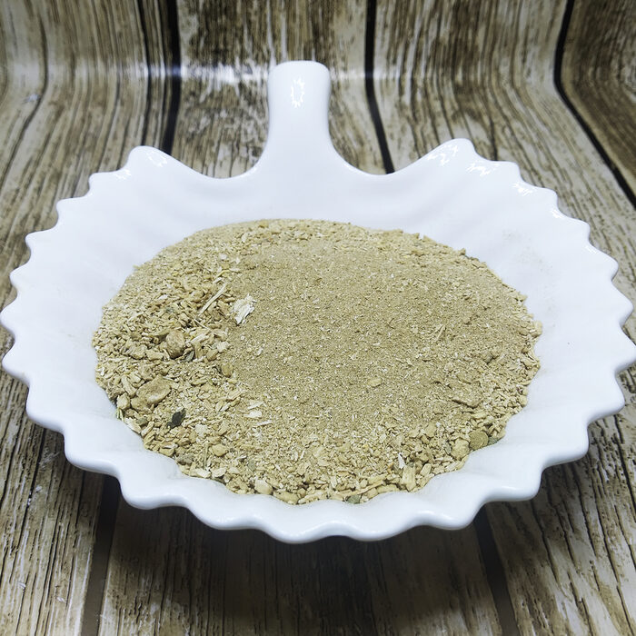Light greenish-beige ground Sarghina powder heaped on a white scalloped dish over a wood-grain surface.