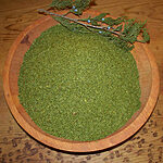 Fine green juniper powder in a wooden bowl beside a juniper branch