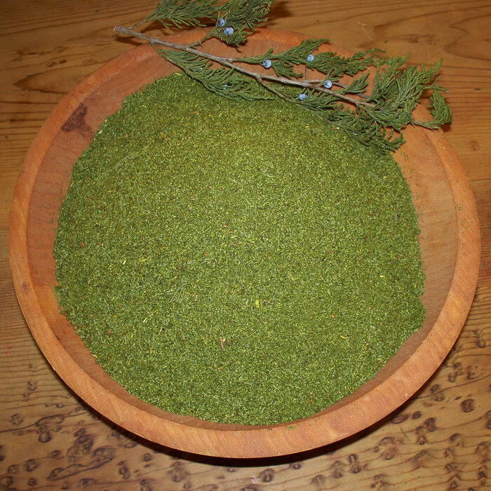 Fine green juniper powder in a wooden bowl beside a juniper branch