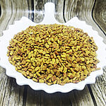 Whole golden fenugreek seeds piled in a white scalloped dish on a wood-grain surface