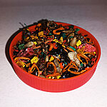 Colourful loose sweet Tfosikha bakhour with dark glossy pieces, dried botanical fragments and bright accents in a red dish.