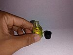 Small clear glass bottle of yellow fragrance essence standing beside a black cap