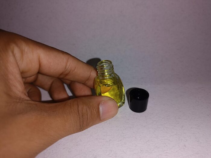 Small clear glass bottle of yellow fragrance essence standing beside a black cap